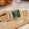 Reloj de cuarzo dorado con esfera cuadrada verde y detalles de circonita, sobre una superficie marrón claro.