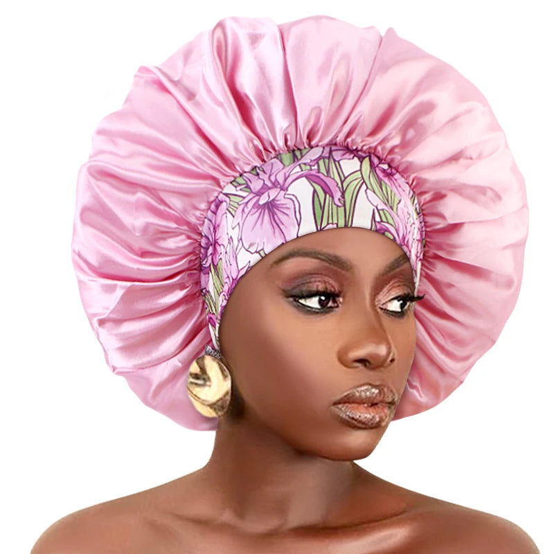 A model wears a pink satin sleep bonnet with a floral patterned elastic band around her head.