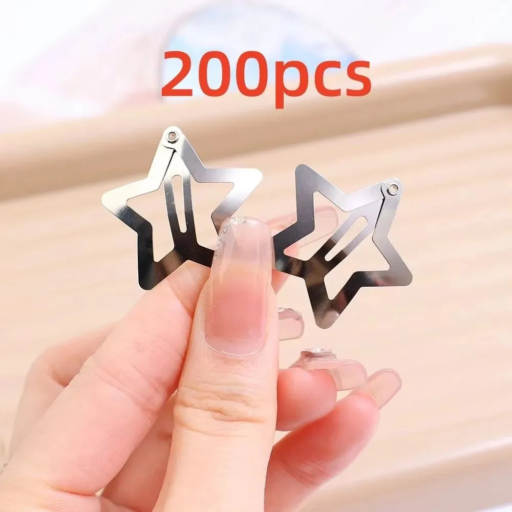 A hand holds silver star metal snap hair clips against a light background.