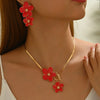 A close-up of a gold floral pendant necklace and matching earrings featuring bright red flowers.