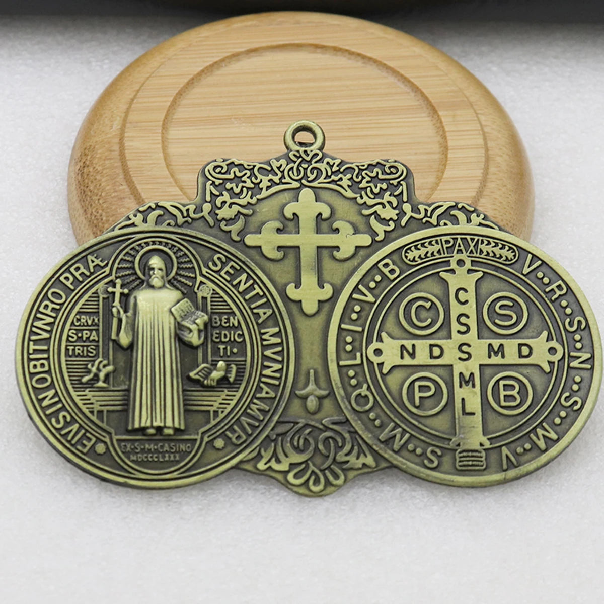 A brass Saint Benedict protection medal featuring a figure and Latin inscriptions, set against a light wooden background.