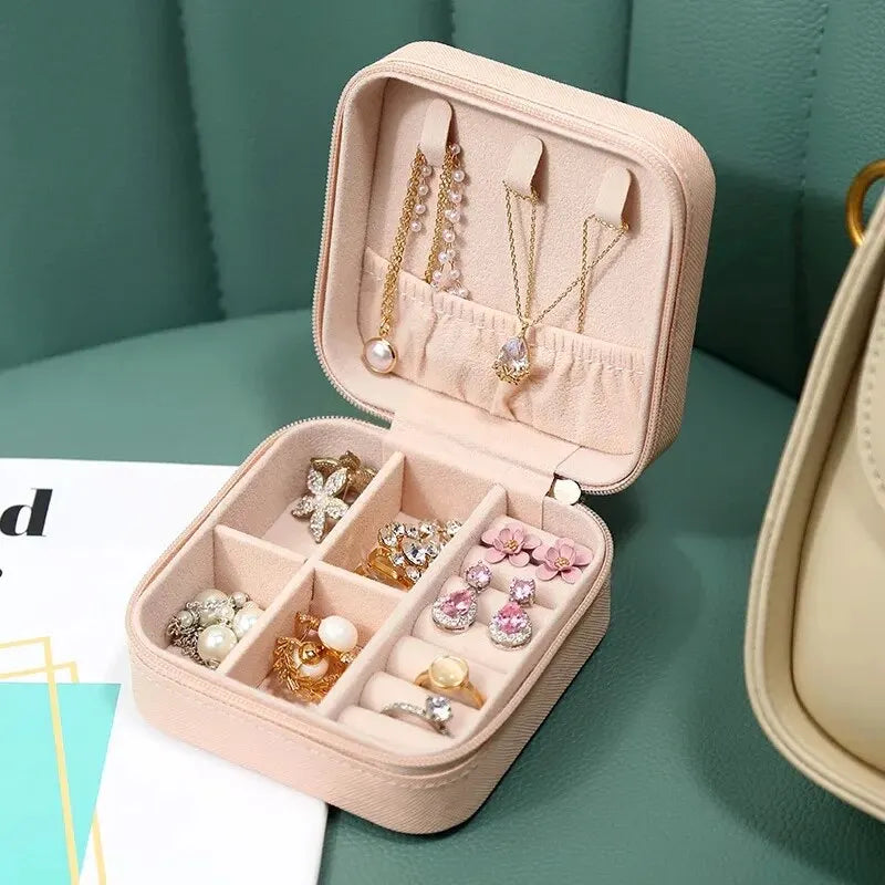 A pink compact leather jewelry travel organizer with compartments for earrings and necklaces is shown on a green surface.