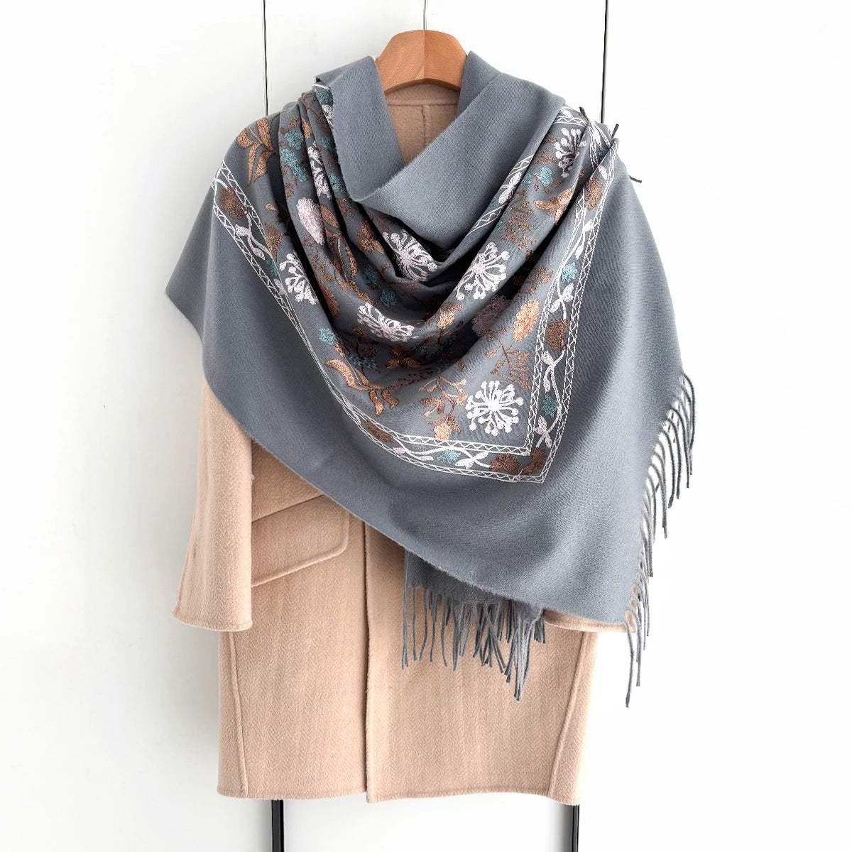 A gray luxury floral scarf draped over a wooden hanger, paired with a beige cardigan.