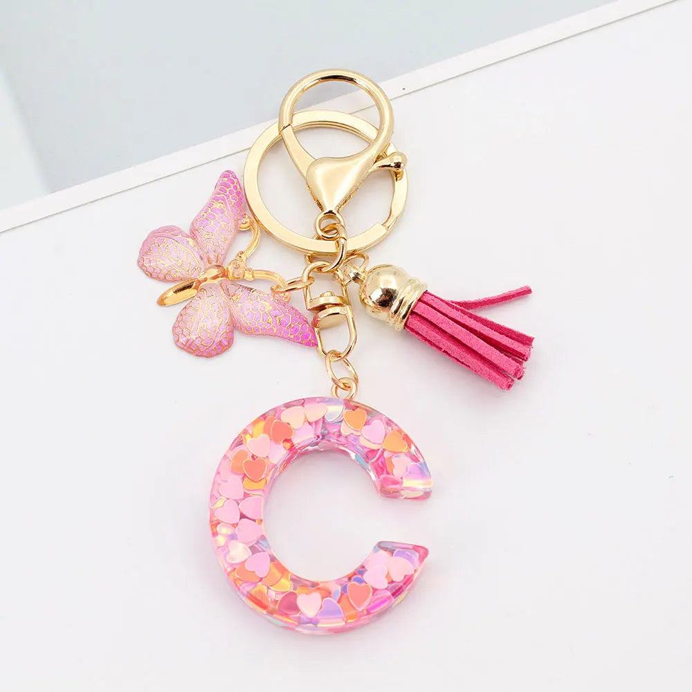 Gold acrylic letter keychain featuring a pink butterfly charm and a magenta tassel
