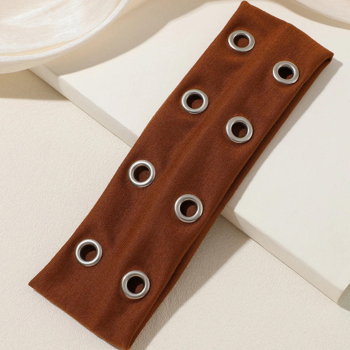 A brown fabric headband with multiple silver metal rings used for fastening.