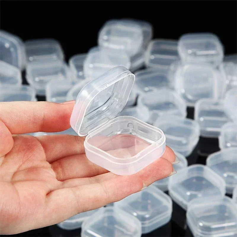 Eine Hand hält eine transparente Mini-Quadratbox zum Aufbewahren von Schmuck und Ohrringen, umgeben von vielen ähnlichen Boxe