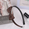 A dark brown grosgrain ribbon hair bow is displayed next to a box and a glass bottle.