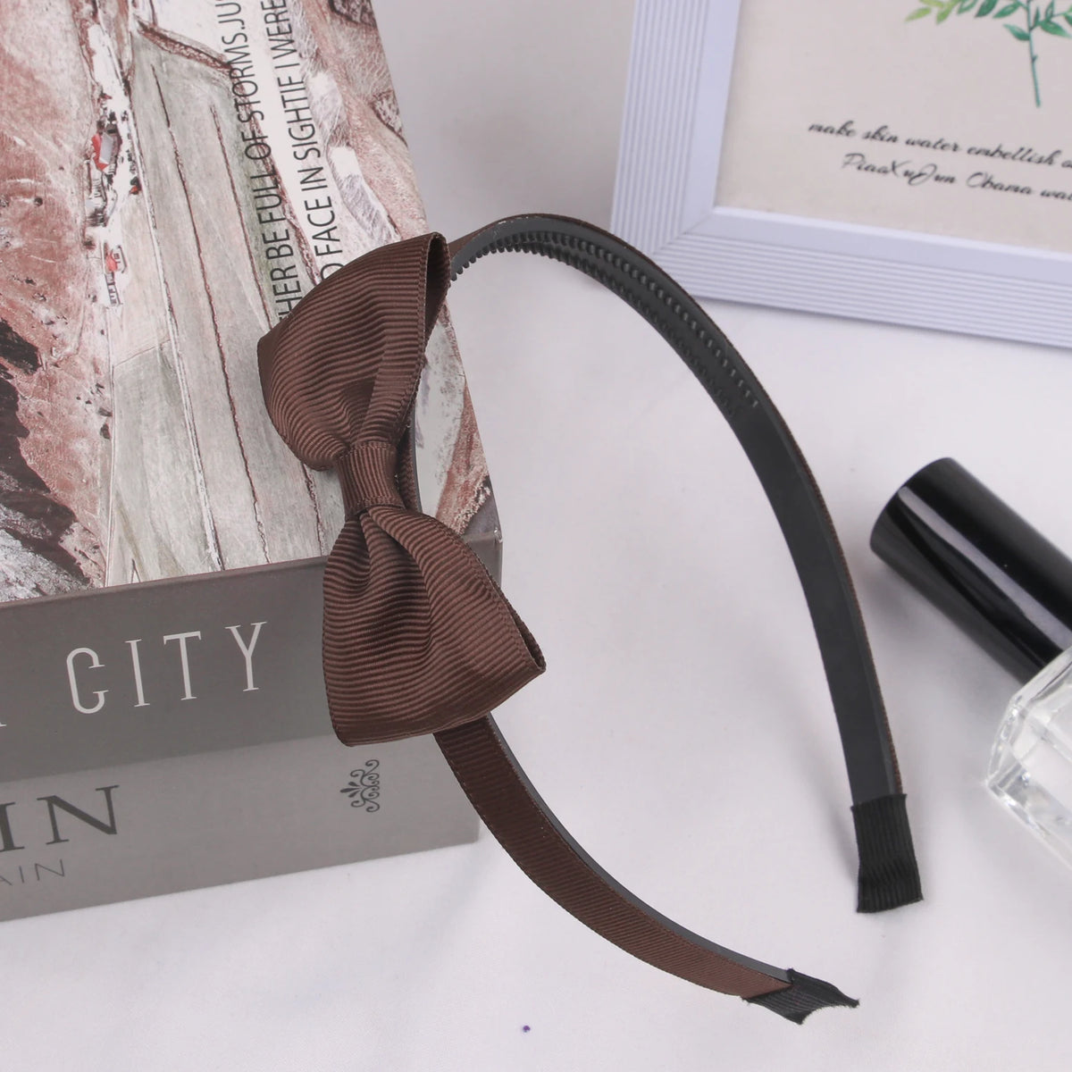 A dark brown grosgrain ribbon hair bow is displayed next to a box and a glass bottle.