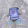 A blue cartoon towel enamel pin with a purple striped design is displayed on a clear, iridescent surface.