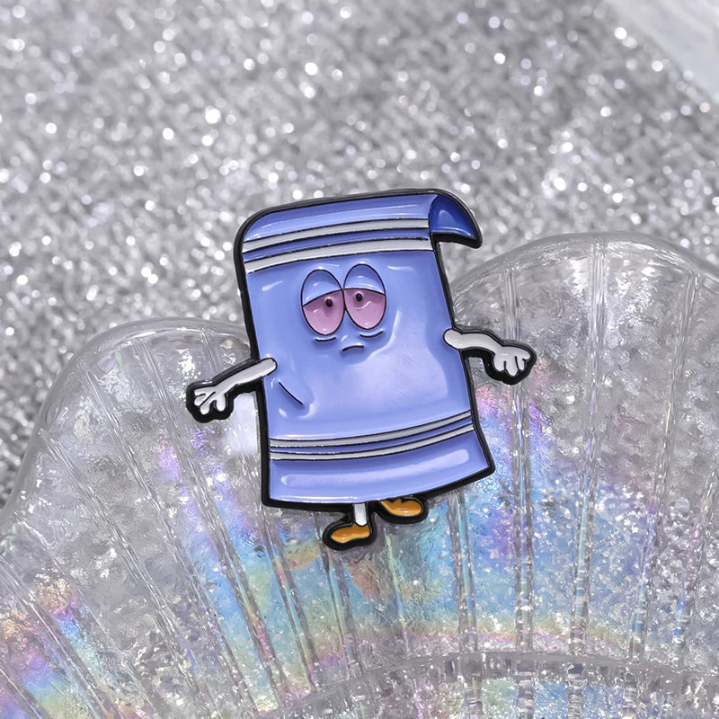 A blue cartoon towel enamel pin with a purple striped design is displayed on a clear, iridescent surface.