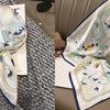 A light blue and white floral print silk scarf tied in a bow, displayed against a gray knitted background.