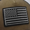 Close-up of a dark olive green tactical baseball cap featuring a black and gray American flag embroidered patch.