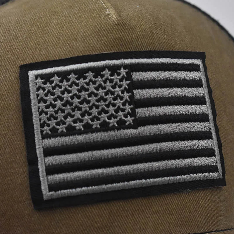 Close-up of a dark olive green tactical baseball cap featuring a black and gray American flag embroidered patch.