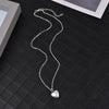 Silver chain necklace with a heart pendant displayed on a black surface.