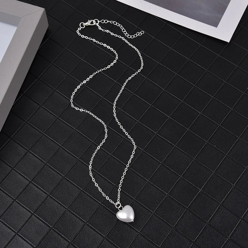 Silver chain necklace with a heart pendant displayed on a black surface.