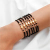 A stack of black and gold resin beaded bracelets worn on a wrist.