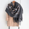 A gray scarf with floral embroidery and dark brown patterns draped over a beige sweater.