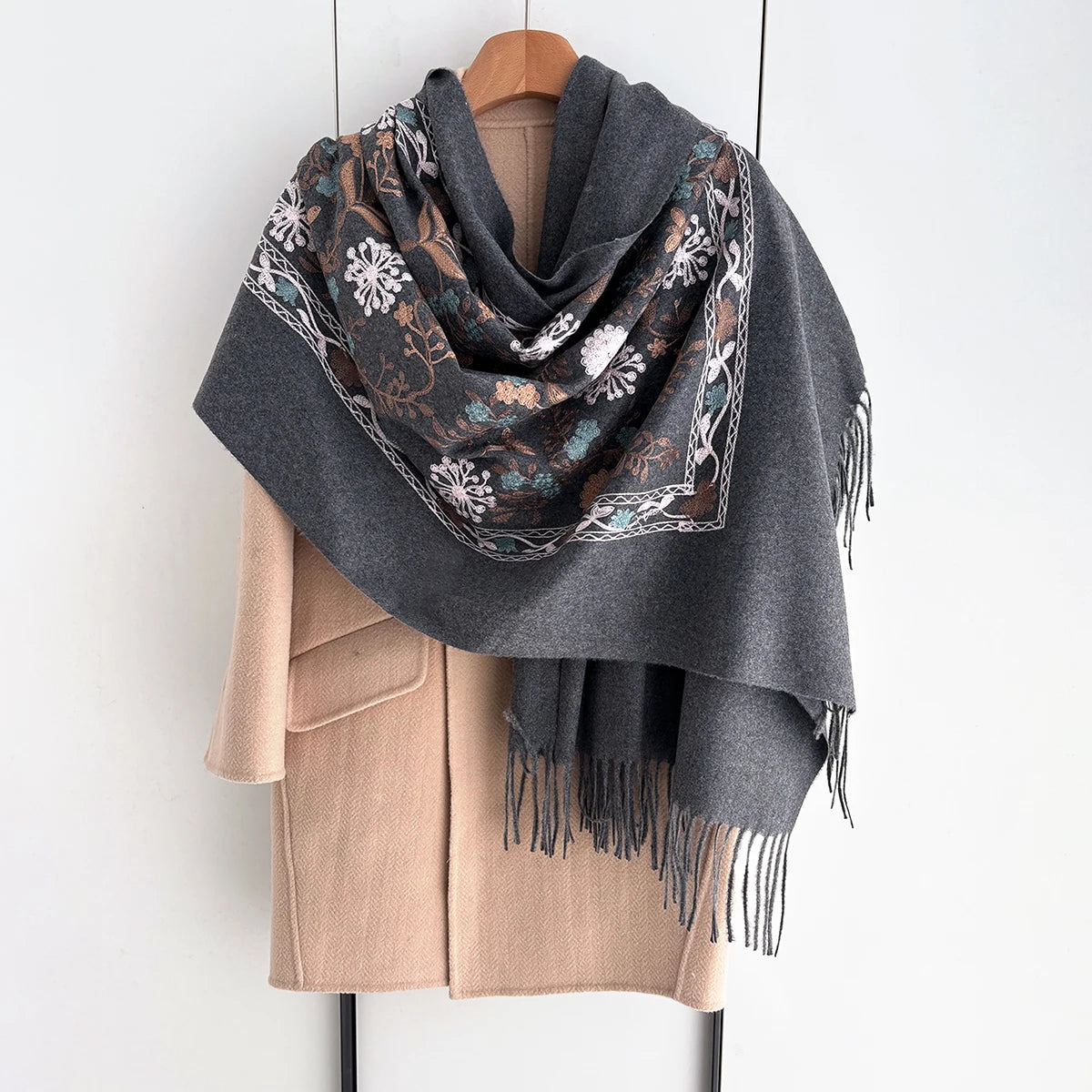 A gray scarf with floral embroidery and dark brown patterns draped over a beige sweater.
