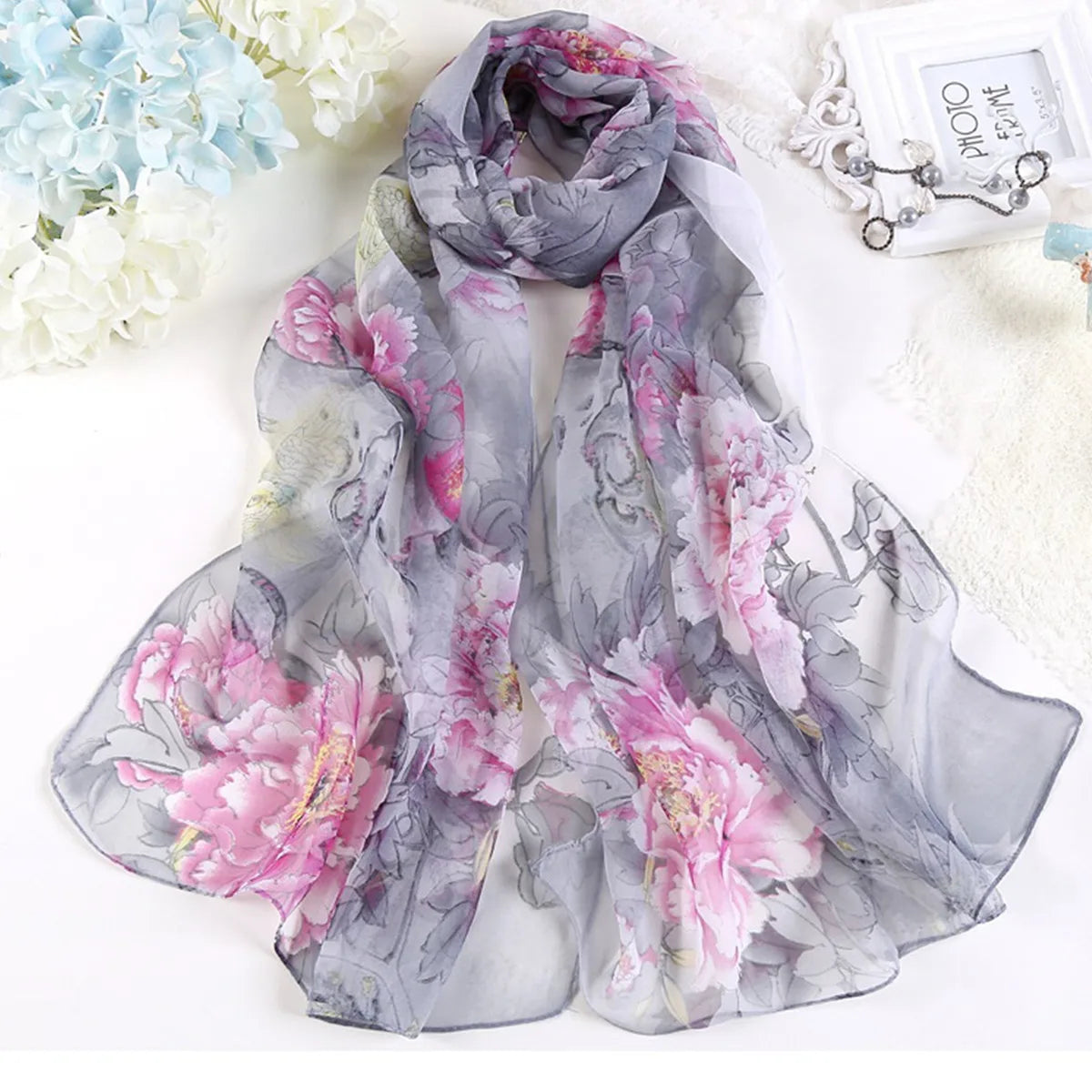 Étoffe florale gris et rose transparente drapée élégamment sur une surface blanche.