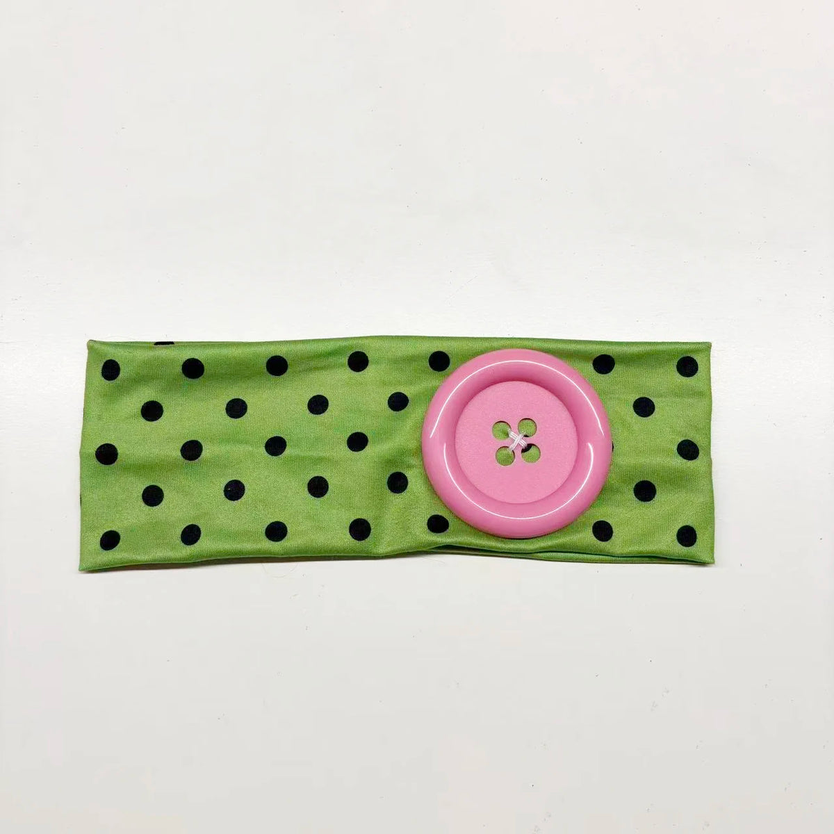 A vintage pink polka dot button headband made of green fabric.