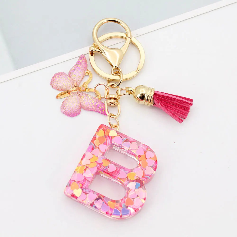 Gold alphabet letter keychain featuring a pink butterfly charm and a magenta tassel