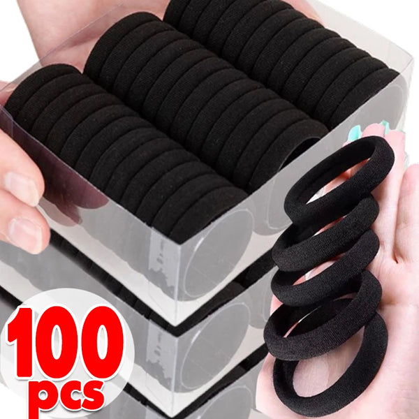 A hand holds a clear container filled with 100 black elastic hair bands for ponytails.