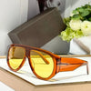 A pair of orange-tinted oversized fashion pilot sunglasses resting on a light wooden surface.