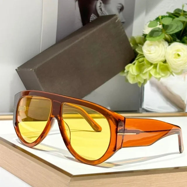 A pair of orange-tinted oversized fashion pilot sunglasses resting on a light wooden surface.