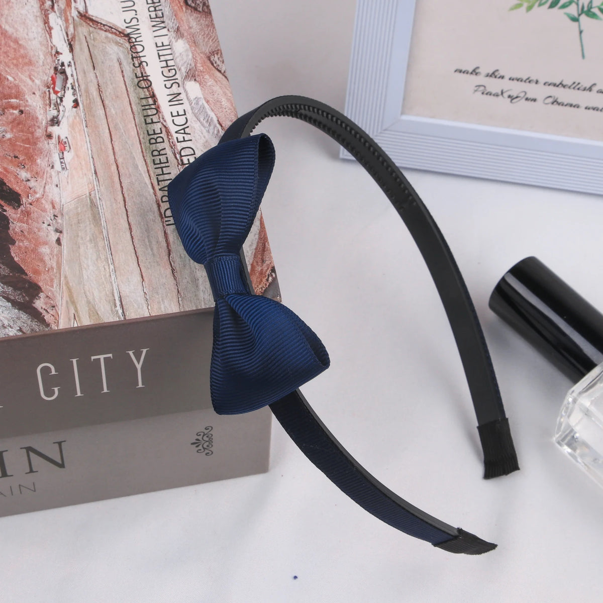 A dark blue grosgrain ribbon hair bow is displayed next to a box and a glass bottle.
