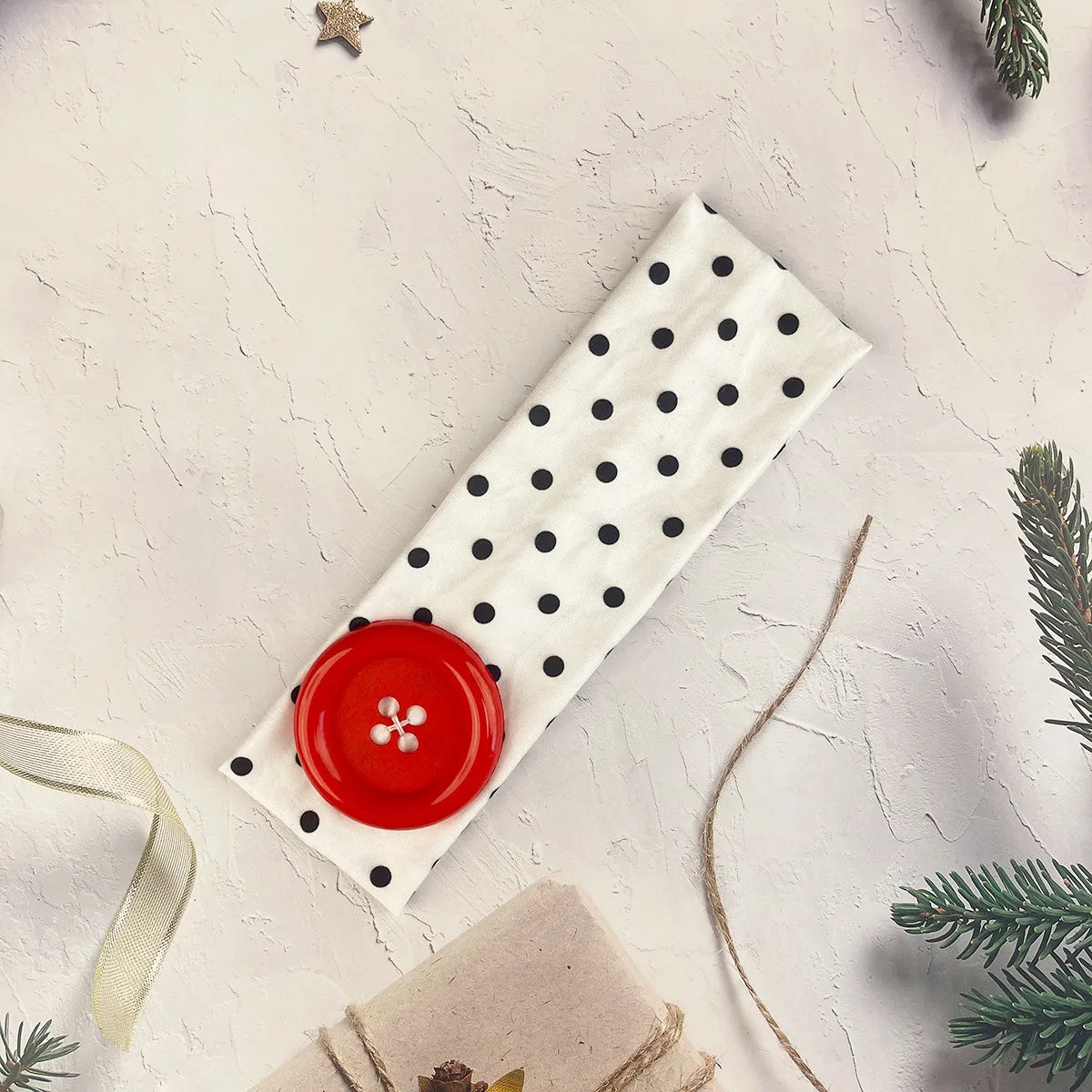 A white polka dot fabric headband with a red button detail is displayed on a light background.