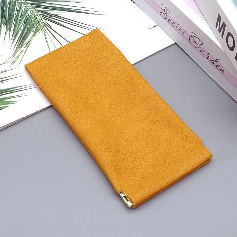 A rectangular mustard yellow PU leather storage bag lying on a gray surface next to some books.