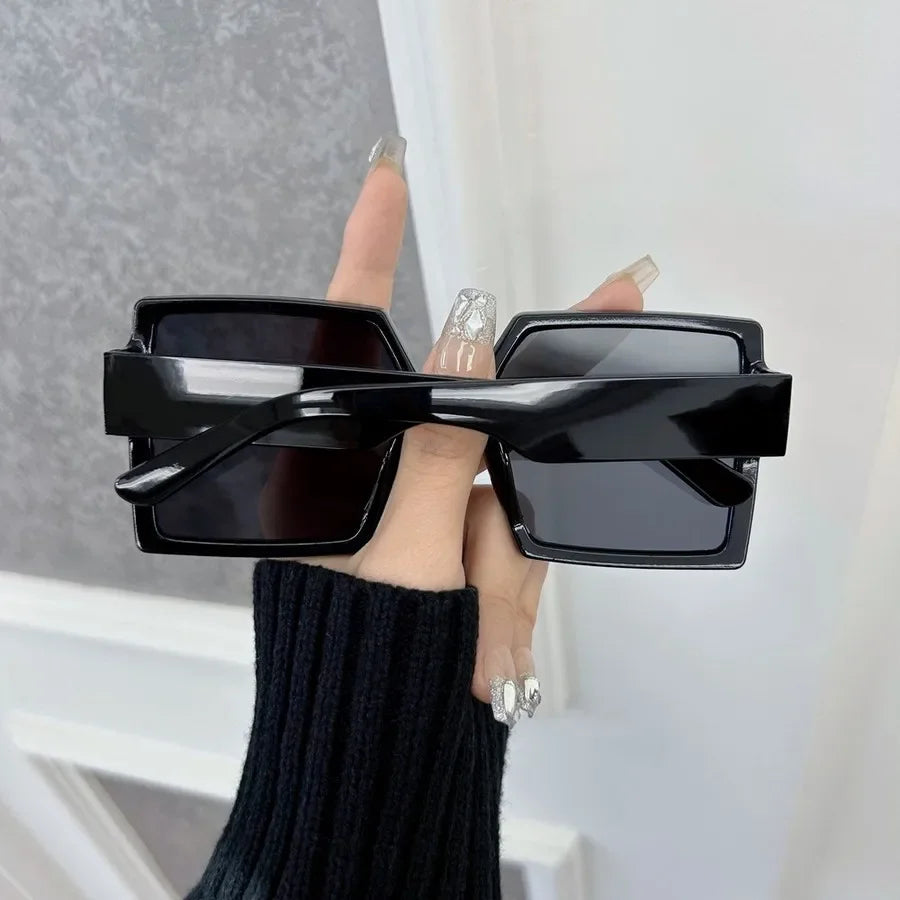 A hand holds a pair of black square mirror sunglasses against a white background.