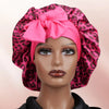 A model wears a pink leopard print satin sleep bonnet with a large bow.