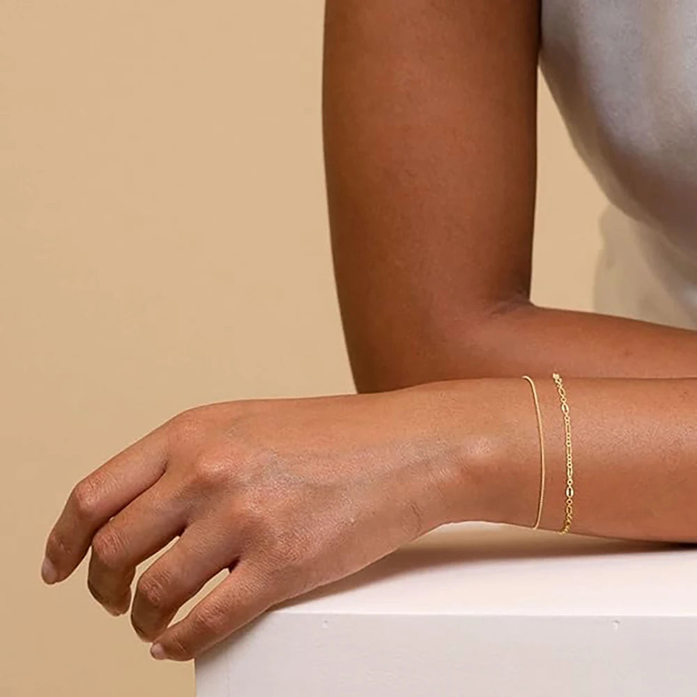 A close-up of a hand wearing a stack of dainty gold plated bracelets on the wrist.