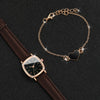 A gold-toned chain necklace with a heart pendant and a brown leather watch is displayed on a dark background.