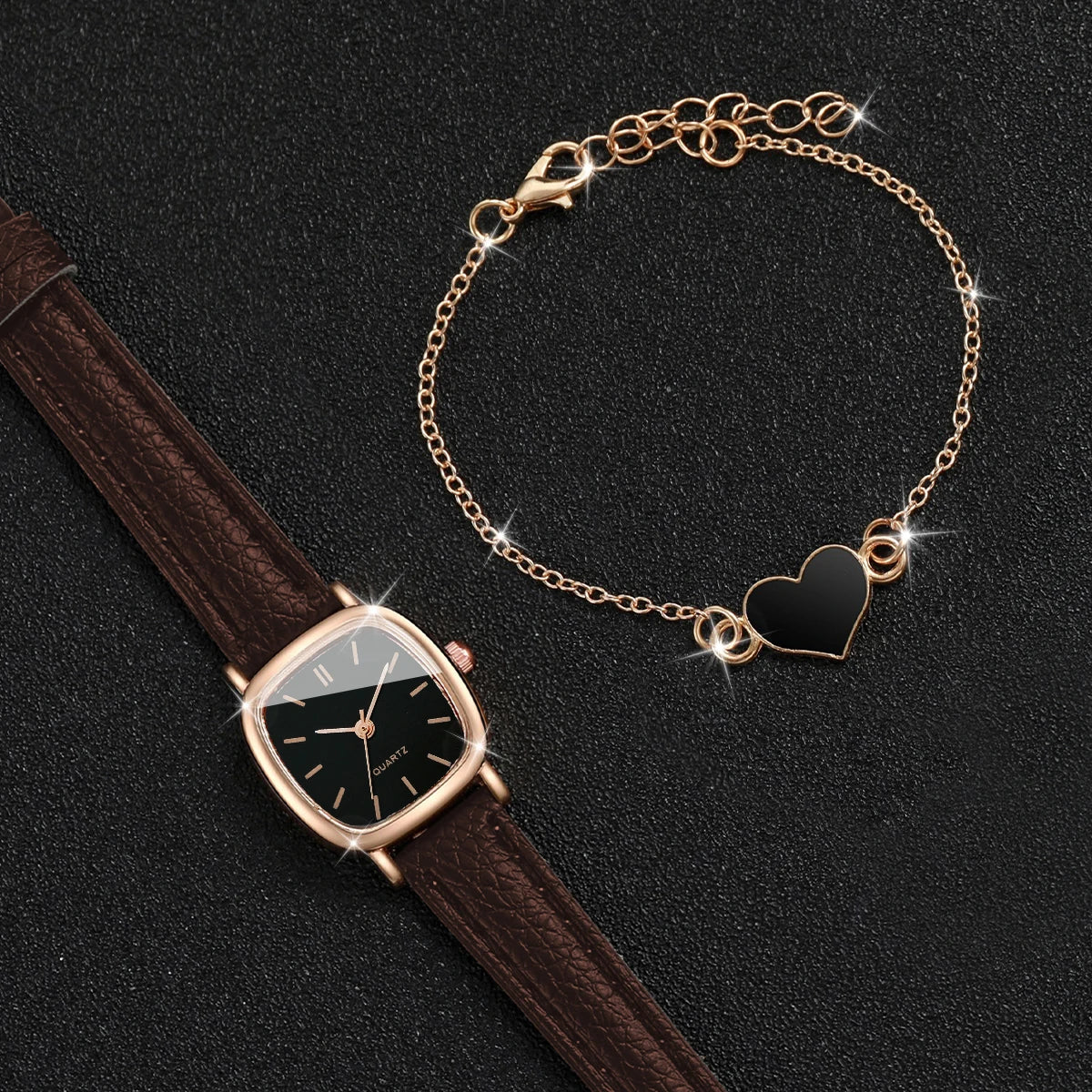 A gold-toned chain necklace with a heart pendant and a brown leather watch is displayed on a dark background.