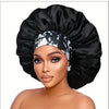A woman wearing an extra large black satin sleep bonnet with a white patterned elastic band
