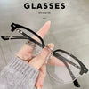 Une main tient une paire de lunettes noires à verres clairs sur un fond gris clair.