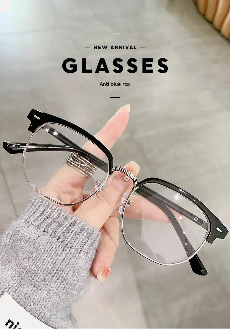 Une main tient une paire de lunettes noires à verres clairs sur un fond gris clair.
