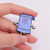 A hand holds a funny cartoon enamel pin featuring a blue character with surprised eyes and striped clothing.