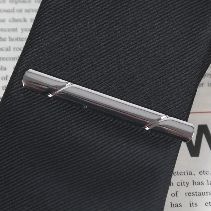 A silver-toned business tie clip with a bar clasp is shown resting on a dark, textured surface.