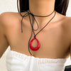 A woman wearing a black rope choker necklace with a red pendant against a light background.