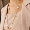 A delicate gold chain necklace with white pearl-shaped charms worn over a beige blazer.