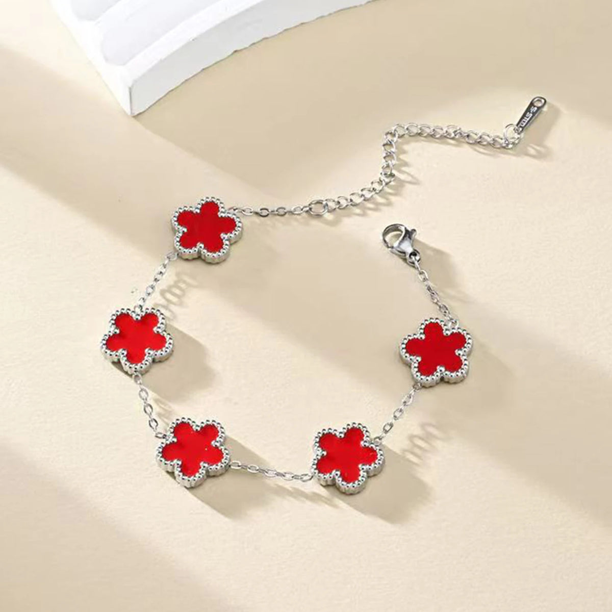 A silver gold plated stainless steel double-sided petal bracelet with red floral charms on a light background.