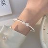 A close-up of a person's wrist wearing a sterling silver charm bracelet with a bow design.