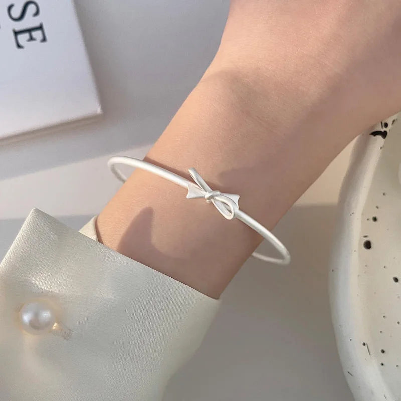 A close-up of a person's wrist wearing a sterling silver charm bracelet with a bow design.