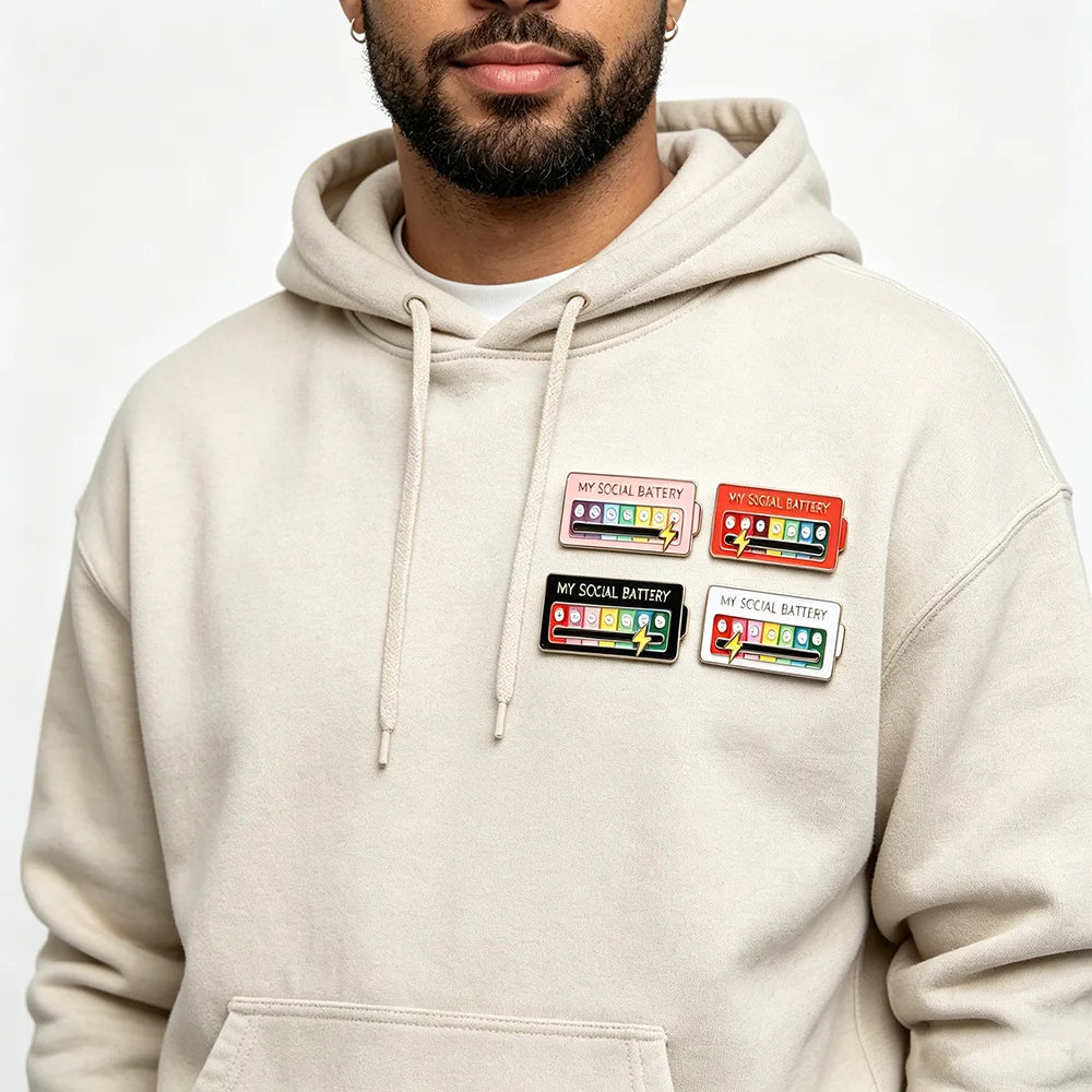 Eine Person trägt einen beigen Hoodie mit mehreren Social Battery Pins auf der Brust.