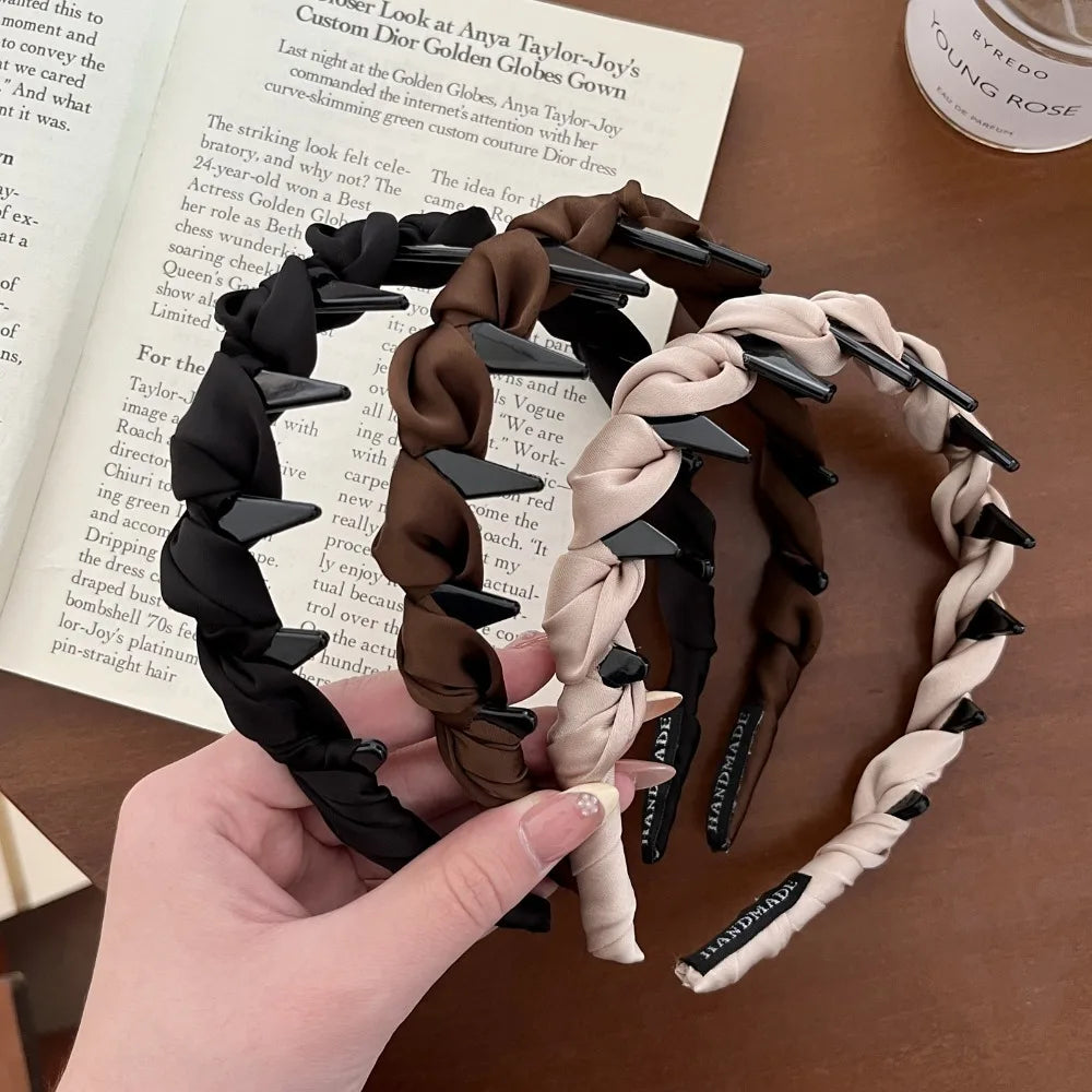 A hand holds a black knotted hair headband with teeth and a beige knotted hair headband with teeth.