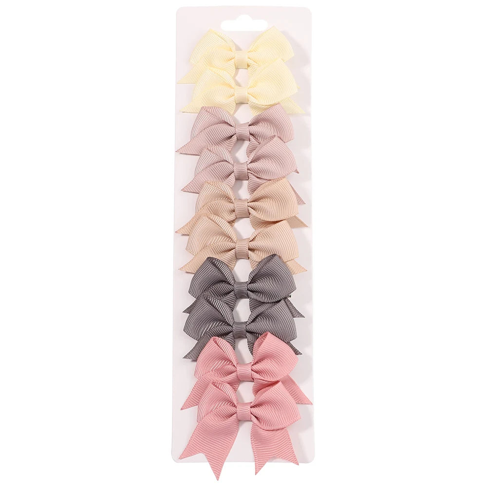 Un set de pinzas para el pelo con forma de lazo de colores sólidos en tonos amarillo, rosa, beige y gris.