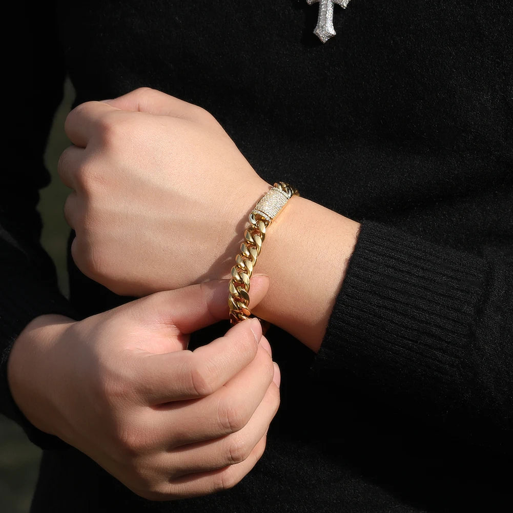 A hand is adjusting a gold-colored stainless steel Cuban link necklace on a wrist, worn under a black sweater.